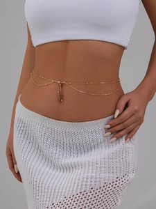 Detail of double-layer gold waist chain with polished beads and tassel on model