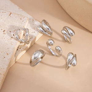 Detailed view of silver liquid metal style rings on a warm beige stone surface