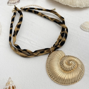 Detail eines goldenen Nautilus-Anhängers an einer Stoffkette mit Leopardenmuster und Verschluss
