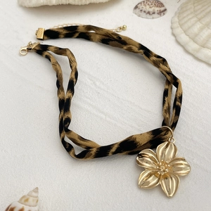 Detail eines Leopardenmuster-Chokers mit einem großen goldenen Blumenanhänger und Verschluss