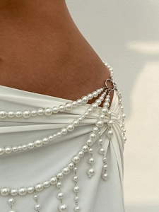 Close-up of layered pearl body chain with hanging tassels on white pleated dress