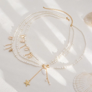 Detail of layered gold body chain with white pearls and hanging sea shell charms