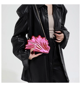 Detail of shell-shaped metallic pink crossbody bag with a gold chain strap on a black jacket