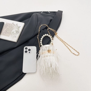Close-up of white feather bucket bag with pearl handle and golden chain on grey background