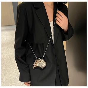Detail einer schneckenförmigen goldenen Metall-Clutch mit Kette auf einem schwarzen Blazer