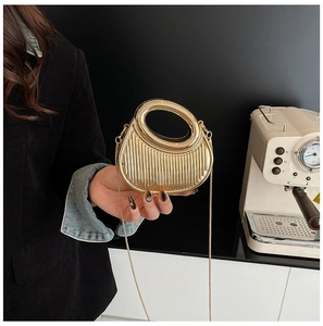 Detail of gold acrylic evening clutch featuring vertical pleats and round hollow handle