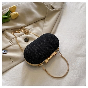 Macro view of oval black evening clutch bag with glitter texture and gold bow clasp