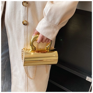 Detalle de un bolso cilíndrico dorado con asa metálica única y correa de cadena fina