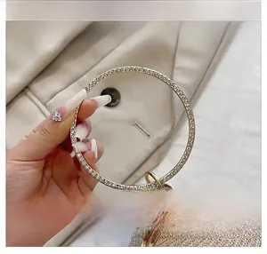 Détail du sac de soirée doré clair avec une poignée circulaire en métal sertie de strass