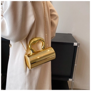 Detalle de bolso de noche cilíndrico dorado con asa artística y correa de cadena