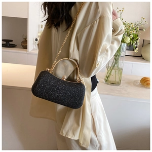 Detail of black glitter evening clutch featuring gold metal handle and chain strap on a bar