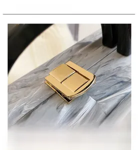 Close-up of polished golden metal lock on marble texture acrylic crossbody bag
