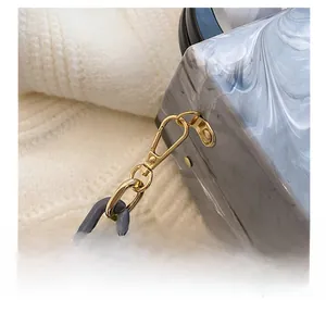 Close-up of detachable gold hook and grey acrylic chain on marble textured bag