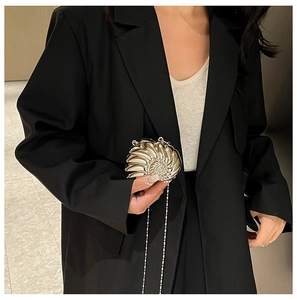 Makroaufnahme der goldfarbenen Abendtasche in Schneckenform mit feiner Metallkette