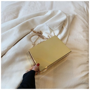 Close-up of golden acrylic box clutch with metal handle and chain on white fabric