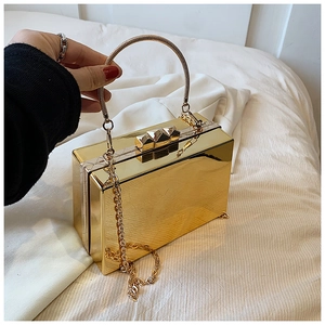 Close-up of a gold mirror-finish acrylic box clutch bag with chain strap and round handle