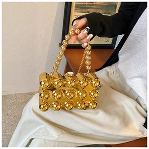 Detail of a modern gold beaded clutch bag featuring spherical metallic elements and a chain strap