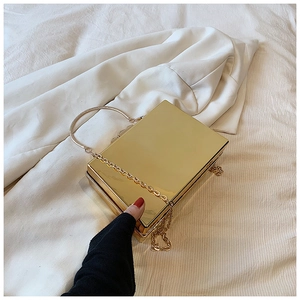 Top view of a gold acrylic box clutch bag with metallic handle and chain strap on fabric