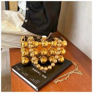 Detailed view of a gold spherical acrylic evening bag with a metallic chain on a book
