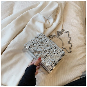 Detail of silver metallic evening clutch bag with hammer texture and round metal handle