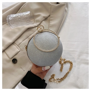 Détail d'un sac de soirée sphérique argenté avec poignée anneau dorée et strass brillants
