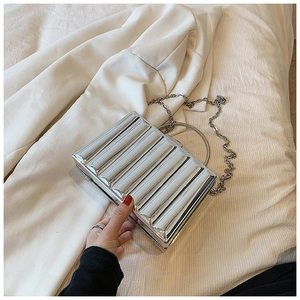 Detailed view of silver metallic hard shell clutch with vertical pleats and round handle
