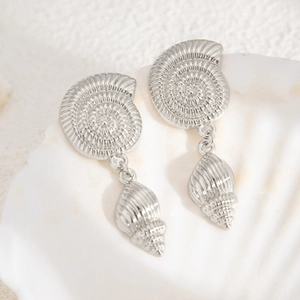 Macro detail of silver starfish earrings with spiral shells on a white decorative shell