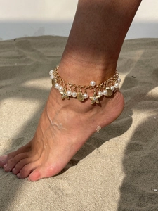 Close-up of bohemian anklet with starfish shell pendants and pearls on sandy beach