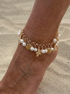 Detail of bohemian gold anklet with starfish and shell charms worn on a sandy beach