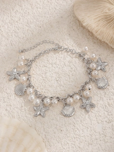 Close-up of ocean-style anklet with silver shells, starfish, and pearls on sand