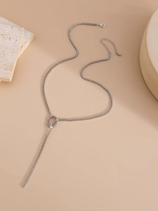 Close-up of a silver box chain Y-necklace draped over stone on a beige background
