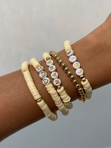 Dettaglio di braccialetti boho a strati con perline dorate e scritte LOVE MAMA