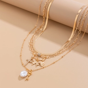Layered gold sequin butterfly necklace with pearls and cross charms on a beige stand