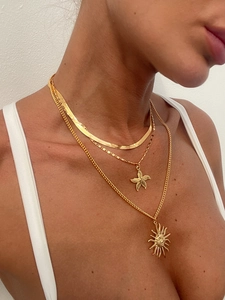 Close-up of layered gold necklaces with snake chain, starfish and sun pendants on model
