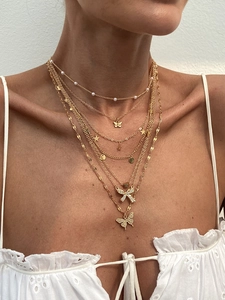 Close-up of layered gold necklace with butterfly charms and pearls on white lace shirt