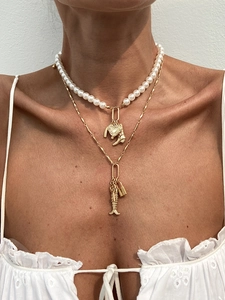 Detail of layered gold necklace with heart and fish pendants on a white shirt