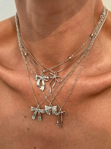 Detail of layered silver bow necklaces with diverse chain styles and pendant designs