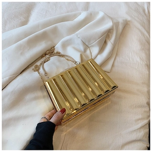Detail of golden wavy texture evening clutch with metal handle and chain strap