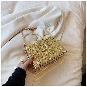 Macro view of golden square clutch featuring hammered metal texture and ring handle