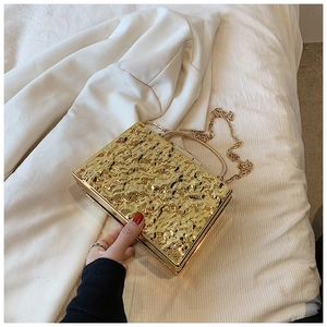 Detail of gold metal clutch with hammer-patterned texture and elegant chain strap