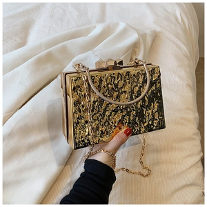 Close-up of gold metallic box clutch featuring ripple texture and chain strap