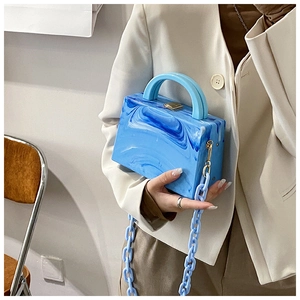 Detail of blue marble acrylic handbag with resin chain and gold clasp on beige suit
