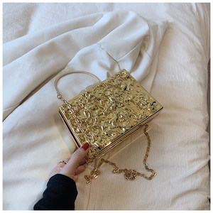 Close-up of golden acrylic box bag with hammered texture, metal handle and chain