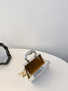 Detail of silver mirror finish evening clutch bag with sleek metal handle and gold chain