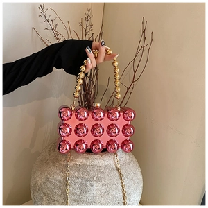 Detail of pink pearlescent bubble acrylic clutch with golden beaded handle and chain strap