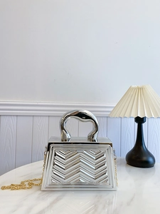 Detail of silver metallic handbag with chevron texture and sleek curved metal handle