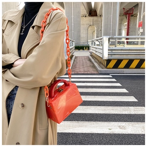 Street style view of orange marble acrylic handbag with thick plastic chain and red handle