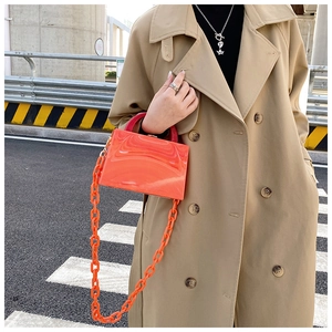 Close-up of orange acrylic handbag with marble texture and chunky chain worn with trench coat