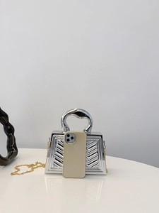 Mini silver trapezoid handbag with V-shaped texture and gold chain for size reference