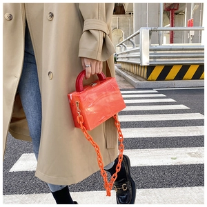 Street style view of an orange marble acrylic box bag with thick chain and red top handle